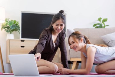 İki kadın evde birlikte egzersiz yapıyor, dizüstü bilgisayarla egzersiz yapıyor, neşeli ve arkadaşça sağlıklı ve aktif bir yaşam tarzını destekliyor..