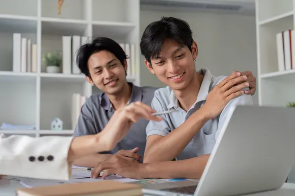 stock image A gay couple planning their finances together at home, using a laptop and documents to discuss future investments and budgeting.