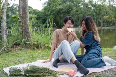 A joyful couple having a picnic by the lake, sharing a moment of laughter and relaxation in a beautiful park. clipart