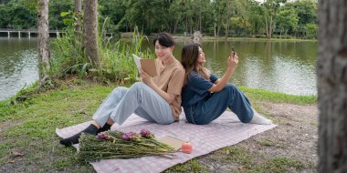 Genç bir çift gölün kenarında huzurlu bir günün tadını çıkarıyor. Biri kitap okuyor, diğeri fotoğraf çekiyor ve piknik battaniyesinde sırt sırta oturuyor..