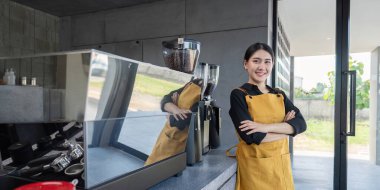 Modern bir kahve dükkanında kendine güveni tam genç bir barista, kolları espresso makinesinin yanında duruyor, müşterilere hizmet etmeye hazır..