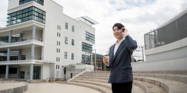 Takım elbiseli, elinde kahve fincanıyla konuşan, modern bir ofis binasının yanında duran kendine güvenen bir iş adamı..