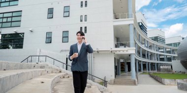 Takım elbiseli genç bir profesyonel modern ofis binasının önünde yürüyor, telefonla konuşuyor ve elinde kahve fincanı tutuyor..