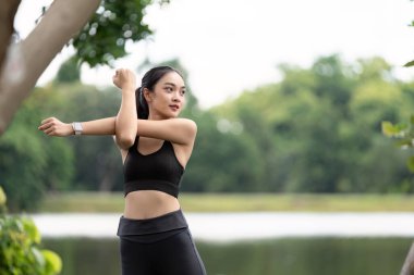 Spor yapan genç bir kadın kollarını açık havada, yemyeşil bir göl kenarında gezdirip sağlıklı ve aktif bir yaşam tarzını teşvik ediyor..
