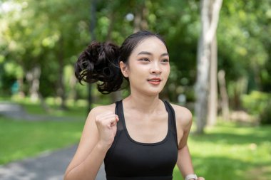 Genç bir kadın parkta koşuyor, spor kıyafetleri giyiyor, formda ve sağlıklı kalıyor, güneşli bir günde arka planda yeşil ağaçlarla dışarıda egzersiz yapıyor..