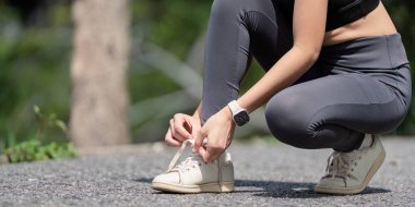 Parkta ayakkabı bağcıklarını bağlayan spor ayakkabıları ve spor ayakkabıları giyen, açık hava egzersizine hazırlanan bir kadının yakın çekimi..