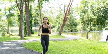Yeşillik ve ağaçlarla çevrili parkta koşan genç bir kadın güneşli bir günün ve açık hava egzersizinin tadını çıkarıyor..