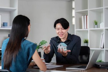 Modellik yapan bir emlakçı modern ofis ortamındaki bir müşteriyle mülkiyet detaylarını tartışıyor..