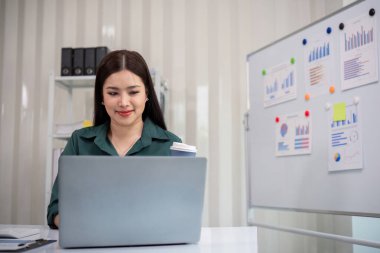 Modern ofis ortamında bir iş kadını, arka planda grafikler ve çizelgeler olan bir dizüstü bilgisayarla çalışıyor..