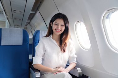 Profesyonel bir iş kadını uçakla seyahat ederken özgüvenle gülümsüyor, modern bir birinci sınıf kamarada oturuyor..