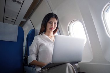 Uçuş sırasında dizüstü bilgisayarında çalışan bir iş kadını modern bir iş ortamında verimlilik ve verimlilik sergiliyor..