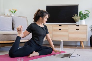 Evde yoga eğitimi alan genç bir kadın. Oturma odasında dizüstü bilgisayar seyrediyor..