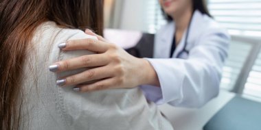 Beyaz önlüklü bir doktor nazikçe elini hastanın omzuna koyar ve modern bir muayenehanede rahatlık ve destek sunar..