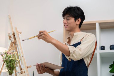 Modern bir stüdyoda, doğal ışık ve yaratıcı ambiyansla çevrili bir tuvalde resim yapan genç bir sanatçı..