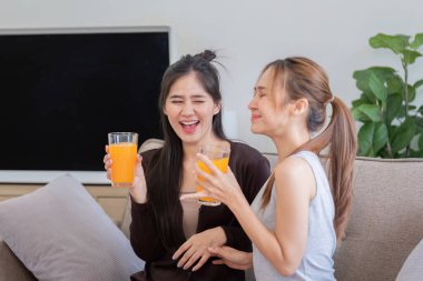 Lezbiyen bir ilişkide gülümseyen iki kadın rahat bir evde portakal suyu içerken keyifli bir anı paylaşıyorlar..
