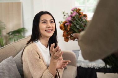 Keyifli bir çift, biri diğerine çiçekler sunarken diğeri de rahat, modern bir oturma odasında hassas bir anı paylaşıyor..