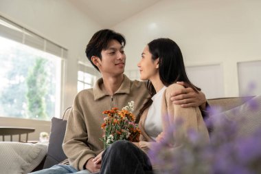 Sevgi dolu bir çift bir kanepede oturuyor, ellerinde bir buket çiçek, ve sıcak, aydınlık bir oturma odasında hassas bir anı paylaşıyorlar..