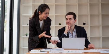 Modern bir ofis ortamında işbirliği yapan iki iş adamı, belgeleri gözden geçirip bir dizüstü bilgisayar üzerinde çalışıyorlar..