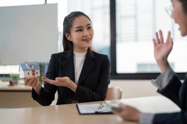 Modern bir ofiste profesyonel bir emlakçı müşteriye ev modelini sunar, mülkiyet detaylarını tartışır ve anlaşmaları bitirir..