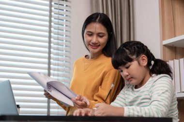 Bir anne kızına ev ödevlerinde yardım eder rahat, modern bir evde bir masada. Sahne aile bağlarını ve eğitimini yakalıyor.