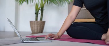 Evde yoga yapan bir kadın rehberlik için dizüstü bilgisayar kullanıyor, evde rahat bir yaşam tarzı, rahatlık ve meditasyon sağlıyor..