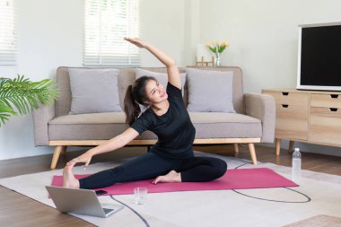 Genç bir kadın şık bir oturma odasında yoga yaparken evinde huzurlu ve sağlıklı bir yaşam tarzı sergiliyor..