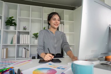 Modern bir ofiste, renk paletleri ve tasarım araçlarıyla çevrili bir bilgisayar üzerinde çalışan yetenekli bir grafik tasarımcısı..