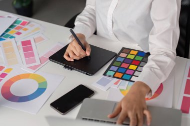 Modern ofis ortamında canlı tasarımlar yaratmak için dijital tablet ve renk paletleri kullanan profesyonel grafik tasarımcısı.