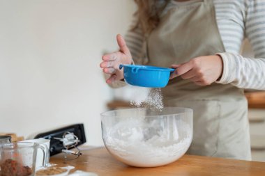 Bir kadın mutfakta bir karıştırma kabına un ekliyor, bir pişirme projesine hazırlanıyor. Bu resim ev yemeklerinin ve mutfak yaratıcılığının özünü yansıtıyor..