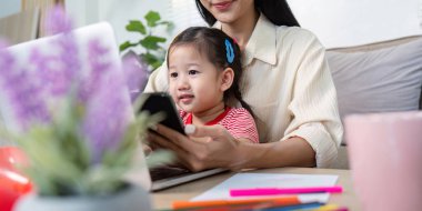 Bir anne, kucağında yürümeye başlayan çocuğuyla evde çalışırken rahat bir oturma odasında dizüstü bilgisayar ve akıllı telefon kullanarak birden fazla iş yapar..