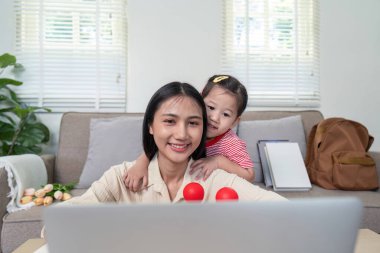 Bir anne ve küçük kızı gülümsüyor ve parlak, rahat bir oturma odasında dizüstü bilgisayar kullanıyorlar..