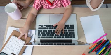 Evde dizüstü bilgisayar ve hesap makinesi kullanarak çalışan bir anne ve kız modern aile yaşam tarzını ve çoklu görevleri sergiliyor..