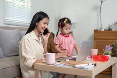 Bir anne, küçük kızı rahat bir oturma odasında onun yanında oynarken dizüstü bilgisayarı üzerinde çalışarak ve telefonla konuşarak birden fazla iş yapar..