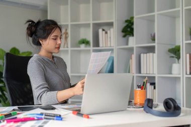 Grafik sanatçısı, masasındaki çeşitli renk şemalarını modern ofis ortamında inceleyerek grafik tasarımında odak ve yaratıcılık göstermektedir..