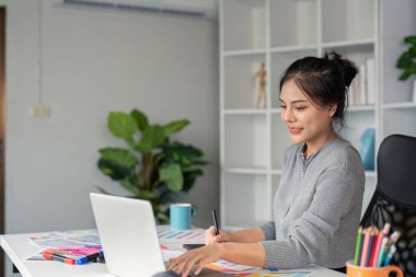 Odaklanmış genç bir bayan grafik tasarımcısı, modern ofis ortamında dizüstü bilgisayarı üzerinde çalışıyor, yaratıcılık ve dijital tasarım becerileri sergiliyor..