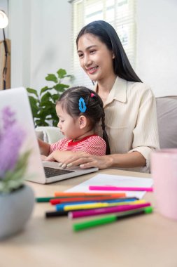 Anne ve kızı evde birlikte vakit geçiriyorlar, neşeli bir aile etkileşimi ve öğrenme anını vurguluyorlar..