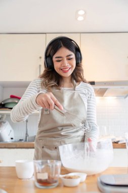 Neşeli kadın kek hamuru çırpıyor kulaklık takıyor, mükemmel bir müzik ve fırın karışımının keyfini çıkarıyor, rahat bir mutfakta..