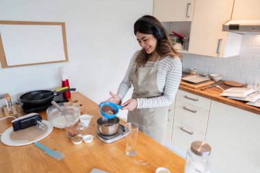 Sıcak bir mutfakta müzik dinlerken yemek pişiren bir kadın, yemek pişirme becerisini ritim ve melodiyle harmanlarken eğleniyor..
