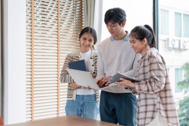 Dizüstü bilgisayarlar ve tabletler kullanarak akademik bir projeyi tartışan çeşitli öğrenci grupları, eğitim alanında takım çalışması ve teknolojiyi temsil ediyor.