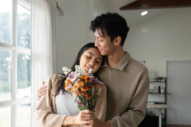 Bir çift bir buket çiçek tutarken sevgiyle kucaklaşır, bir sevgi ve birliktelik anı yakalar..