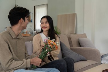Bir çift oturma odasında bir buketle anlamlı bir değiş tokuşu paylaşıyor, sevgi ve samimiyet sergiliyorlar..