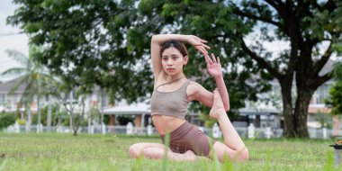 İleri düzey yoga yapan genç bir kadın parkta poz veriyor, esneklik ve konsantrasyon gösteriyor..