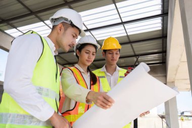 Bir inşaat alanının planlarını birlikte inceleyen mühendislerden oluşan bir ekip, takım çalışması ve tasarım planlamasına odaklanıyor..