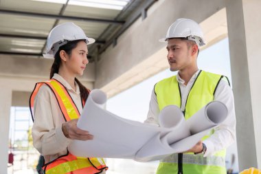 İnşaat planlarını inceleyen iki mühendis, projenin tasarım ve koordinasyonuna odaklanıyor.
