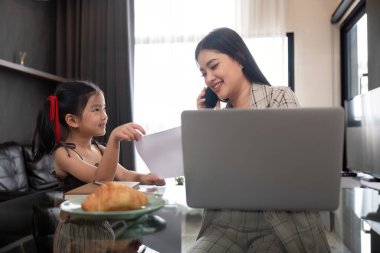 Evde çalışan bir anne ve kız uzaktan çalışma ve aile etkileşimini vurgulayarak iş birliği yapıyorlar..