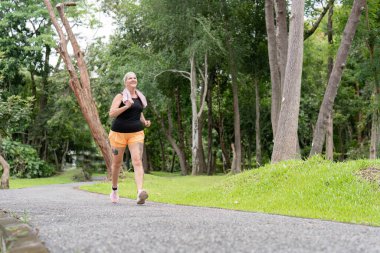 Ağaçlar ve çimlerle çevrili yemyeşil bir parkta yürüyüş yapan bir kadın güneşli bir günün tadını çıkarıyor..