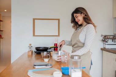 Kendini işine adamış Asyalı bir kadın şık bir mutfakta malzemeleri karıştırıyor, keyifli ve enfes bir tarif yaratıyor..