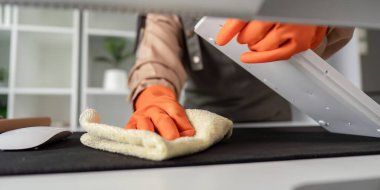 Temizlikçi eldivenli eller klavyeyi bezle siliyor, ofis masasında hijyeni teşvik ediyor.