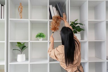 Asyalı temizlikçi ofis raflarını temizlemek, tozsuz ve düzenli bir çalışma alanı oluşturmak için toz bezi kullanıyor.