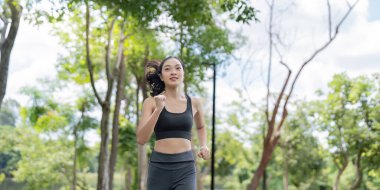 Yeşillik bir parkta enerjik bir şekilde koşan Asyalı kadın aktif ve sağlıklı bir yaşam tarzını benimsiyor..